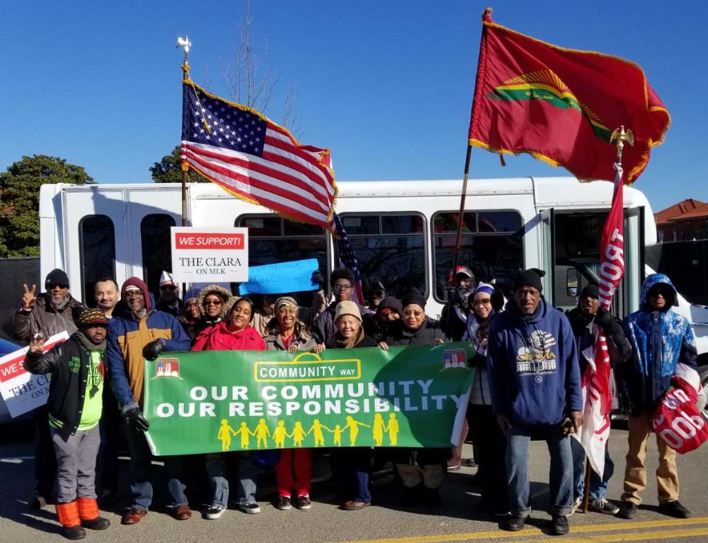 Image of MAVA members holding banner and flag standing in front of the bus